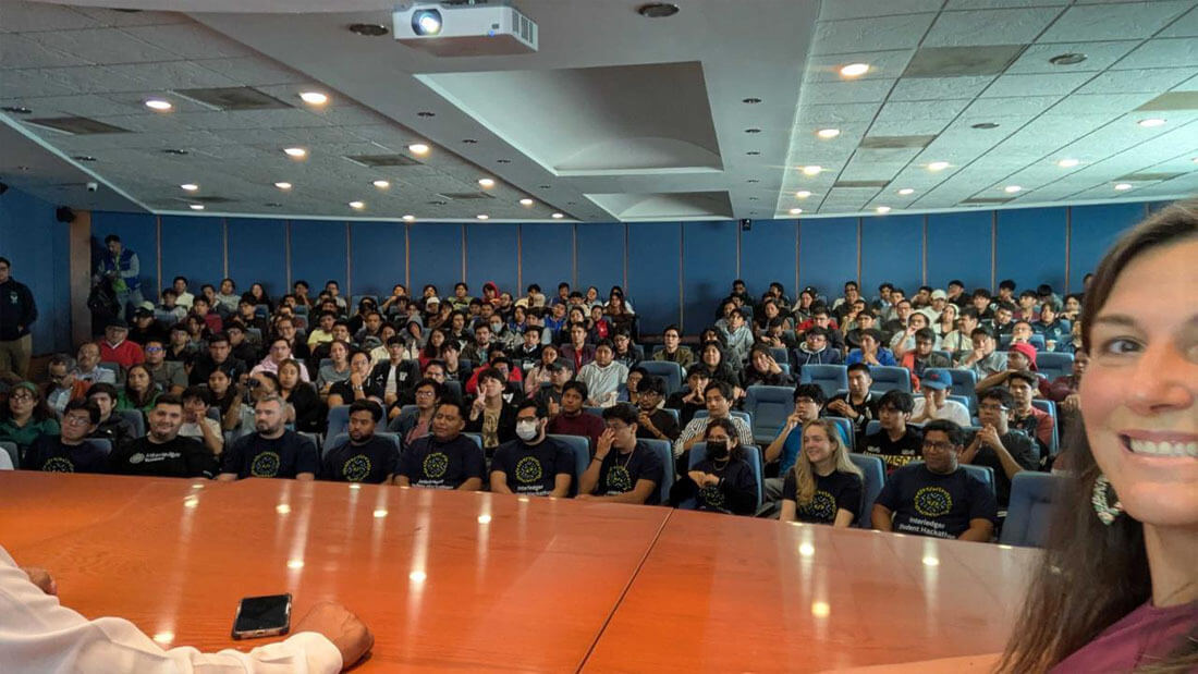 A university lecture hall filled with students seated throughout the room, with the hackathon mentors sitting in the front row.